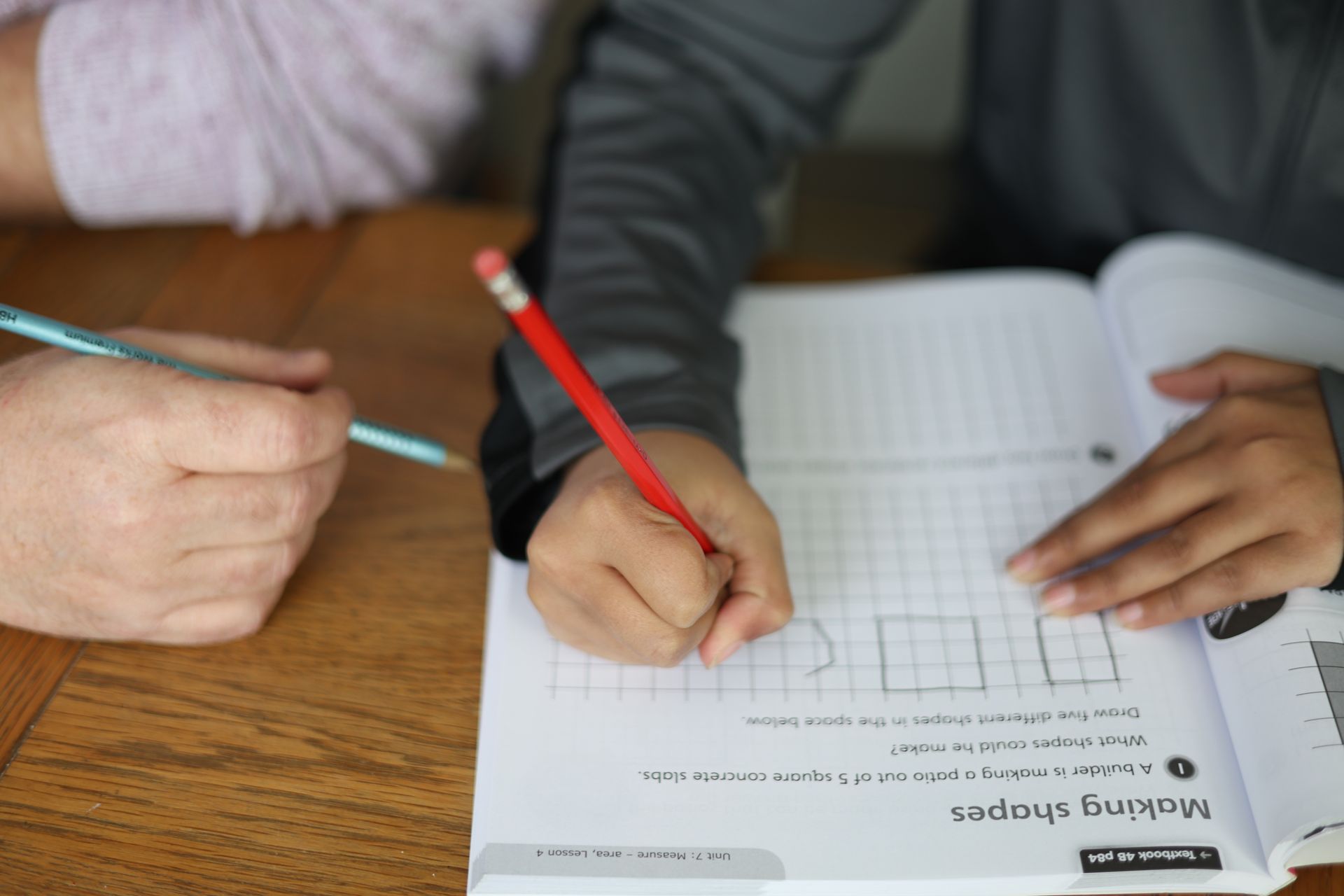 A child is writing on a piece of paper with a red pencil