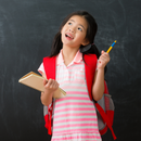 A little girl is holding a notebook and a pencil in front of a blackboard.