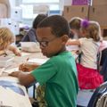 A young boy wearing glasses sits at a table with other children