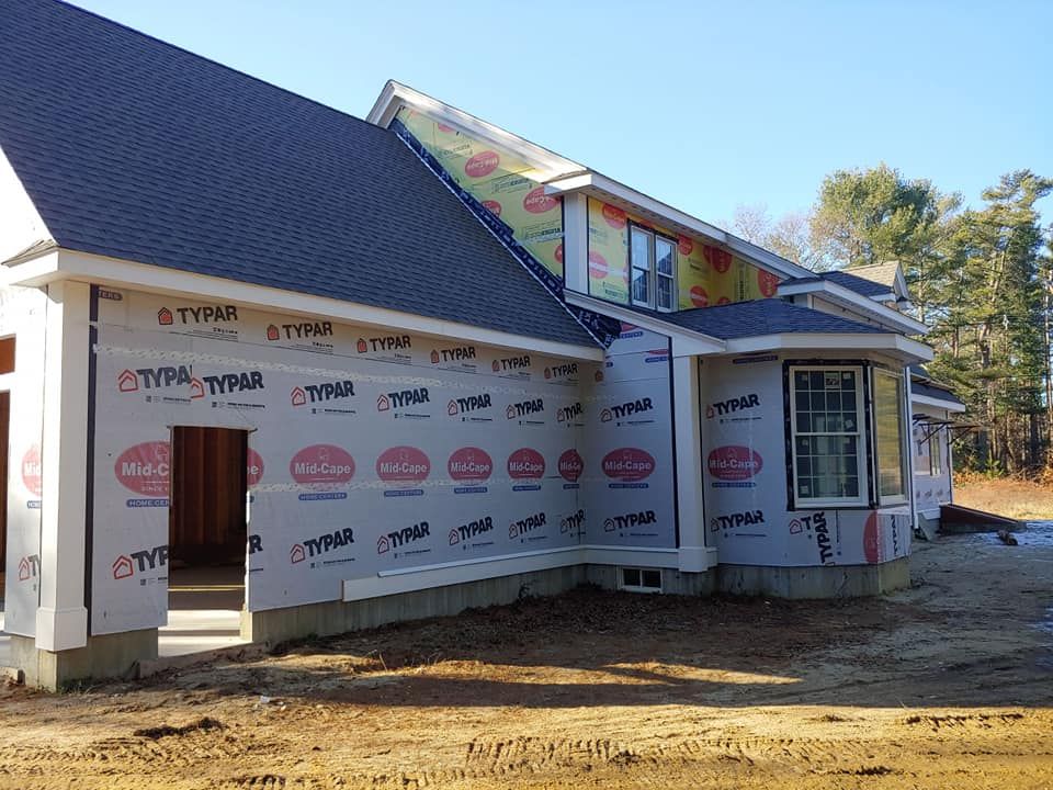 New home under construction; Tyvek wrap covers exterior walls; windows and roof in place.