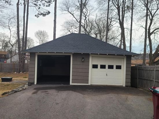 Two-car detached garage with asphalt driveway. One door open, the other closed. Gray siding, tan trim, dark roof.