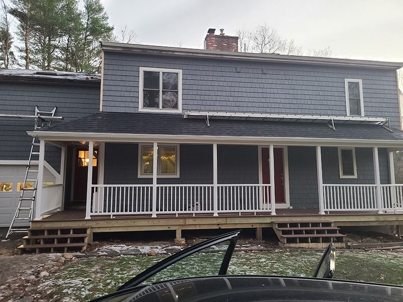 Two-story house with gray siding, white trim, porch, and a partially open garage door. A ladder leans against the house.