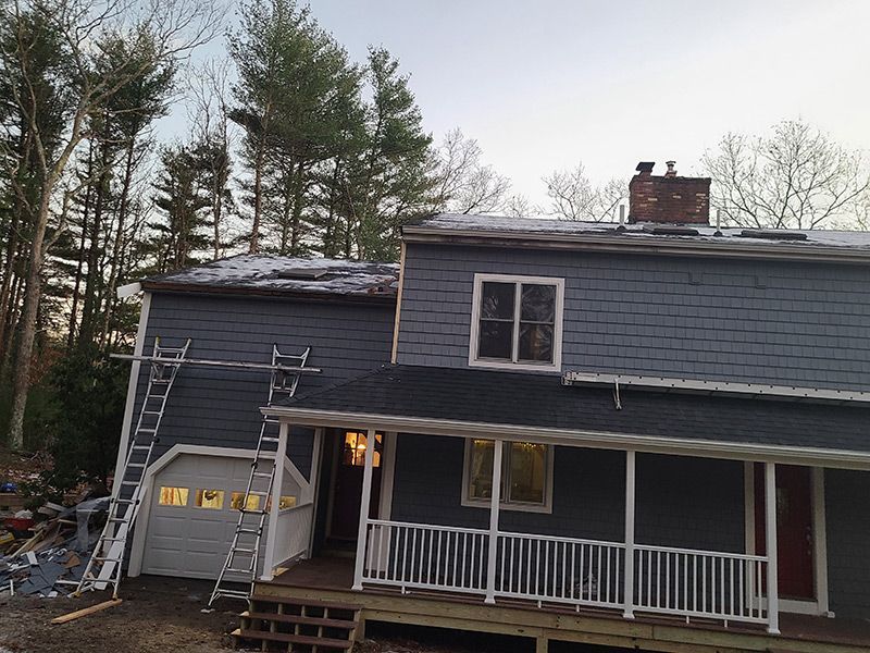 House with blue siding and a porch; ladders propped up for roof work.