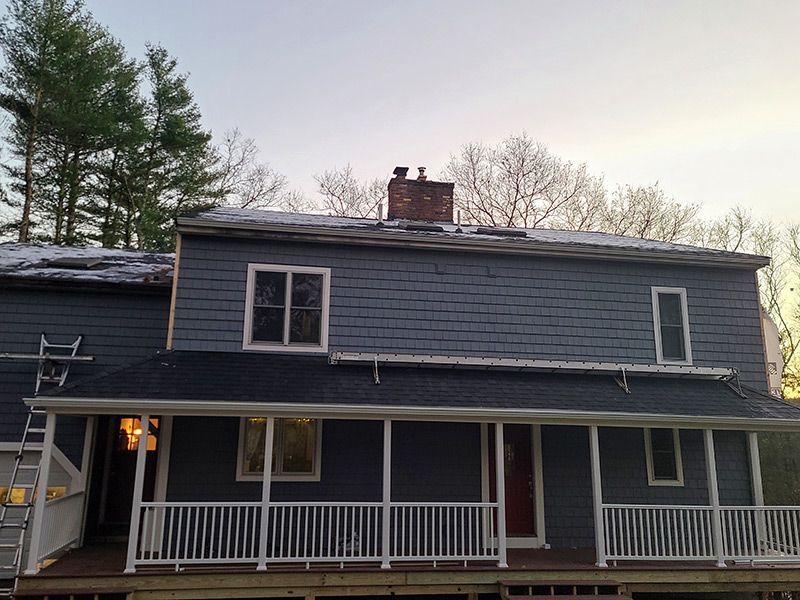 Two-story house with blue siding, a porch, and a brick chimney under a dusky sky.