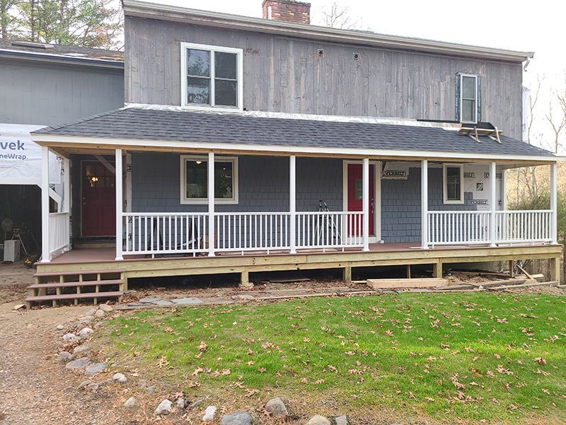 House with gray siding and white porch railing; red door. Construction underway.
