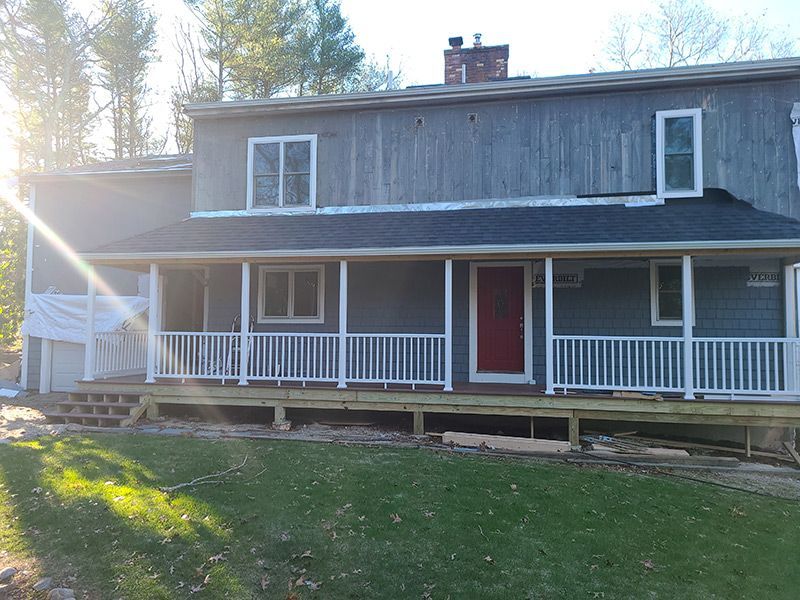 Two-story house with a blue-gray exterior, red front door, white porch railing, and a wooden deck.