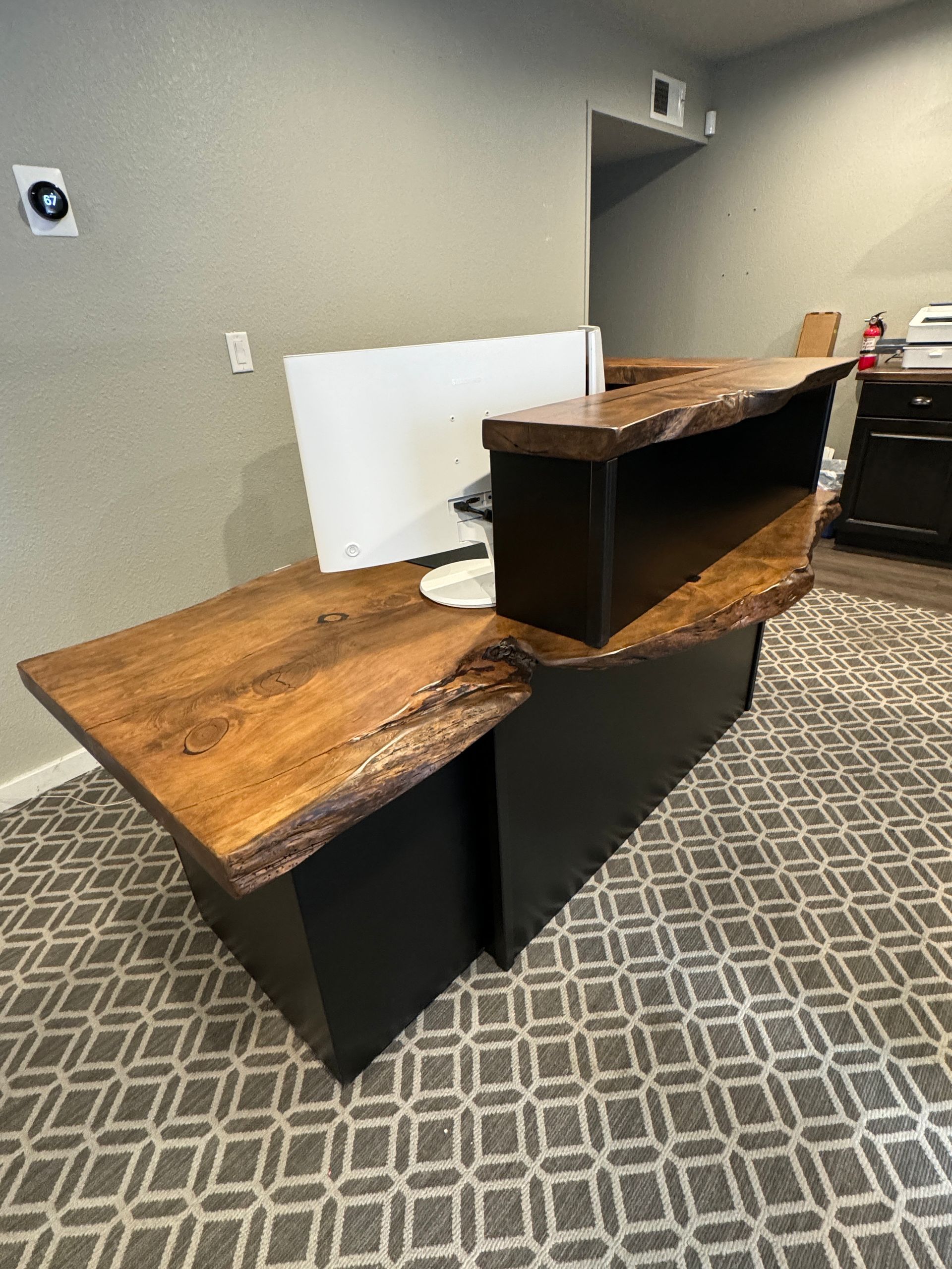 Wooden desk with live edge, black cabinets, and white monitor in a gray room.