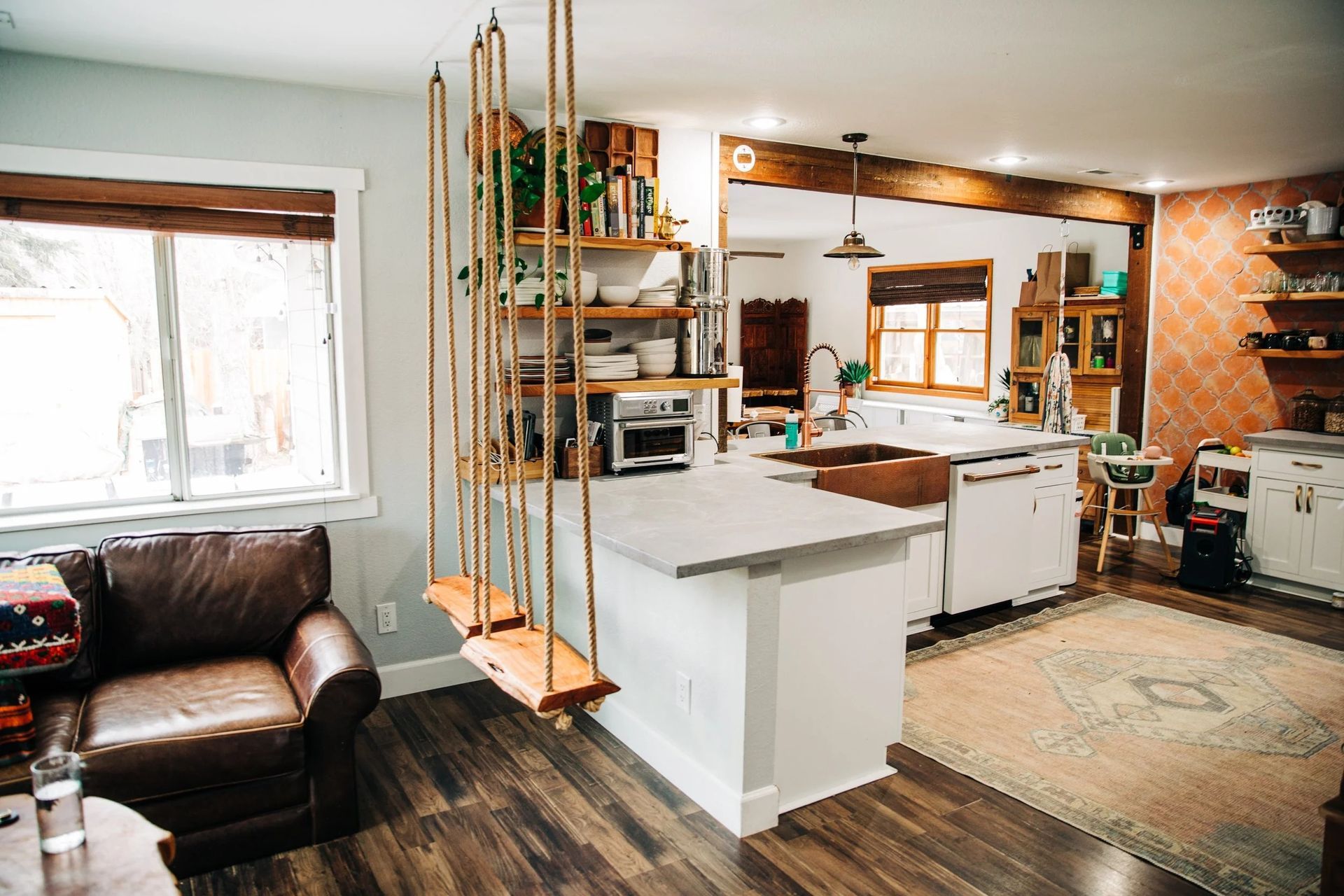 Open-concept kitchen and living room with a hanging shelf unit and rope swings.