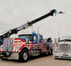 Tow truck painted with the American flag, crane extended, parked next to another truck.