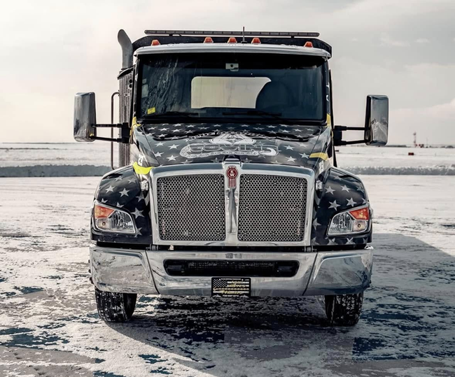 Front view of a black semi-truck with American flag design on snow.