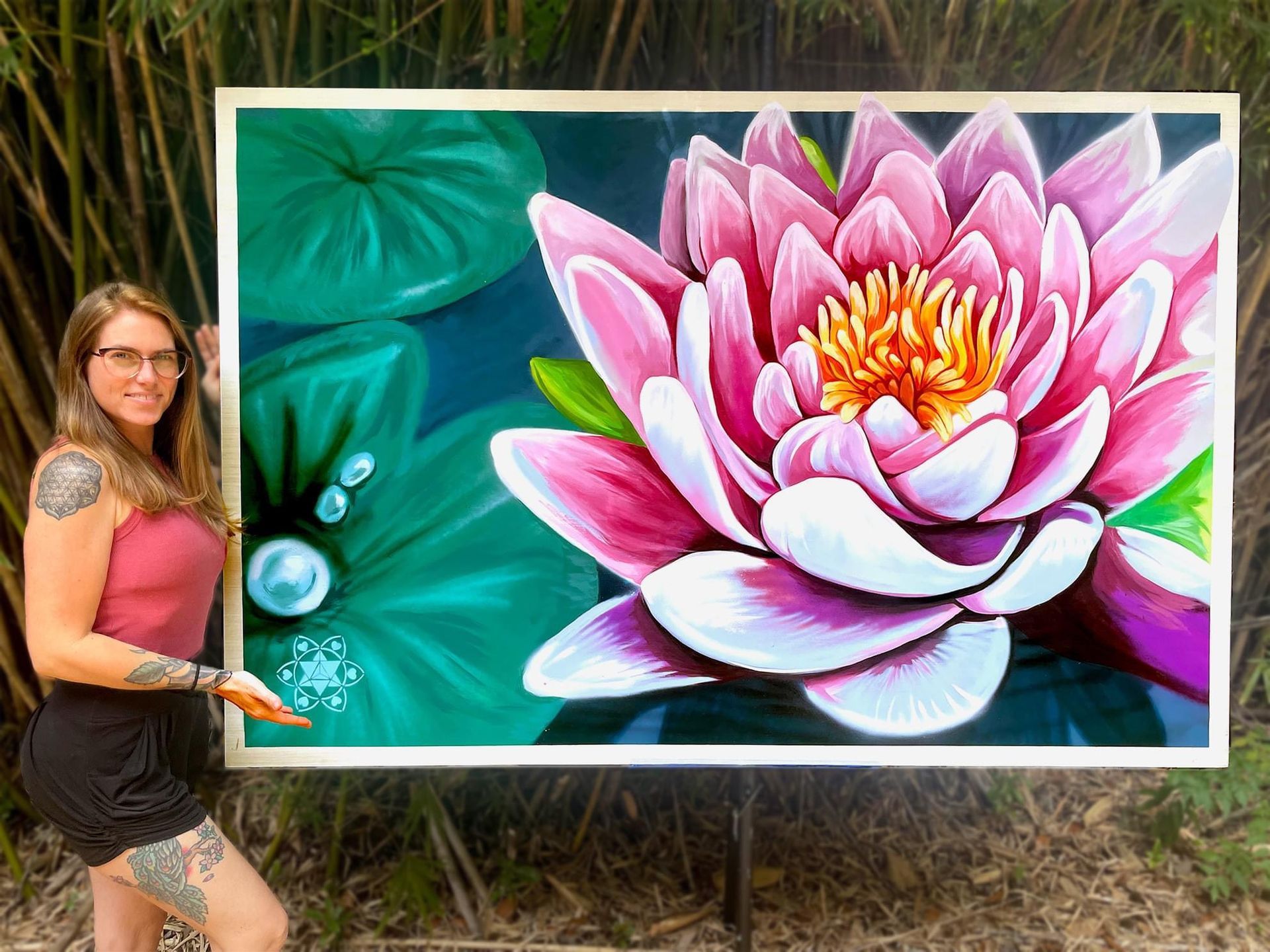 Spray paint and hand painted lotus flower created during a painting performance at the Inspire to Rise Mural Reveal event. The painting has a large lotus flower in vibrant pinks, purples, and yellows. Danielle Cleary of Heartspace Art stands next to the large 6' x 4' painting.