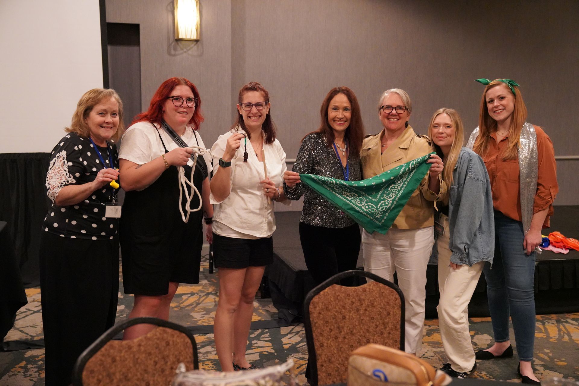 Group of people holding a green scarf, smiling. Indoors, likely at an event or conference.