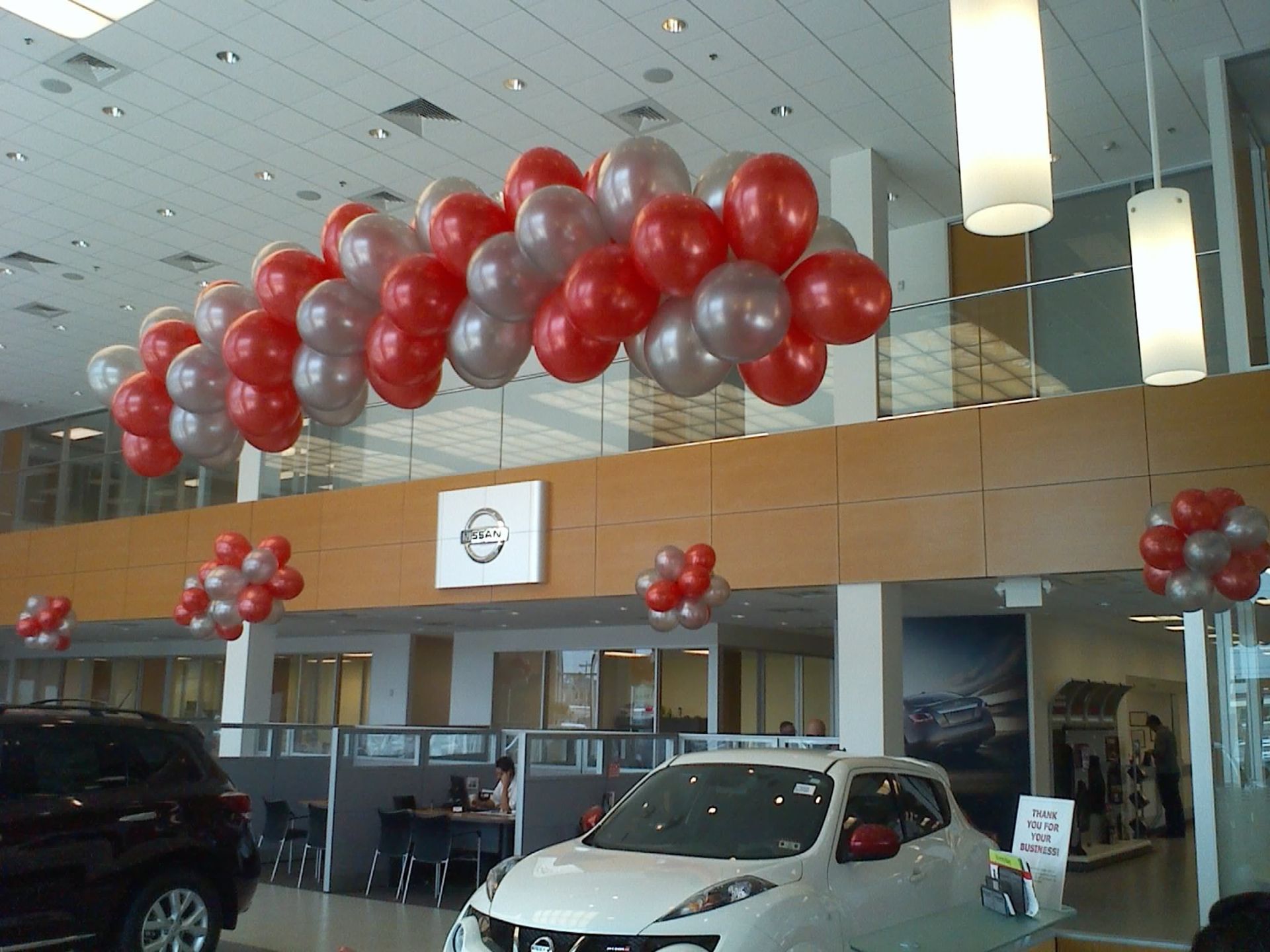 A car dealership with red and silver balloons hanging from the ceiling