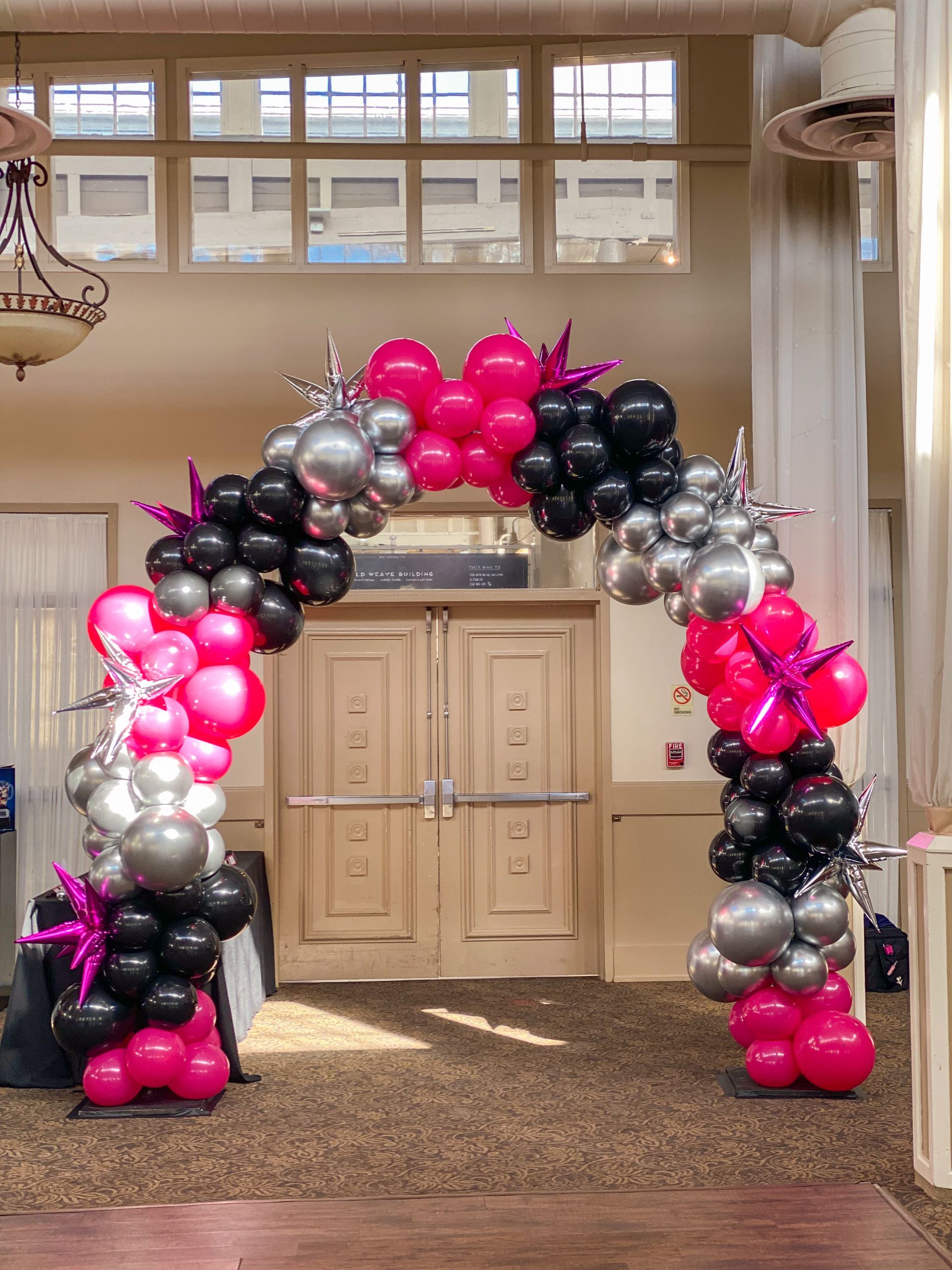A large arch made of pink , black , and silver balloons in a room.