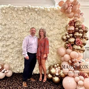 A man and a woman are standing in front of a wall of balloons.