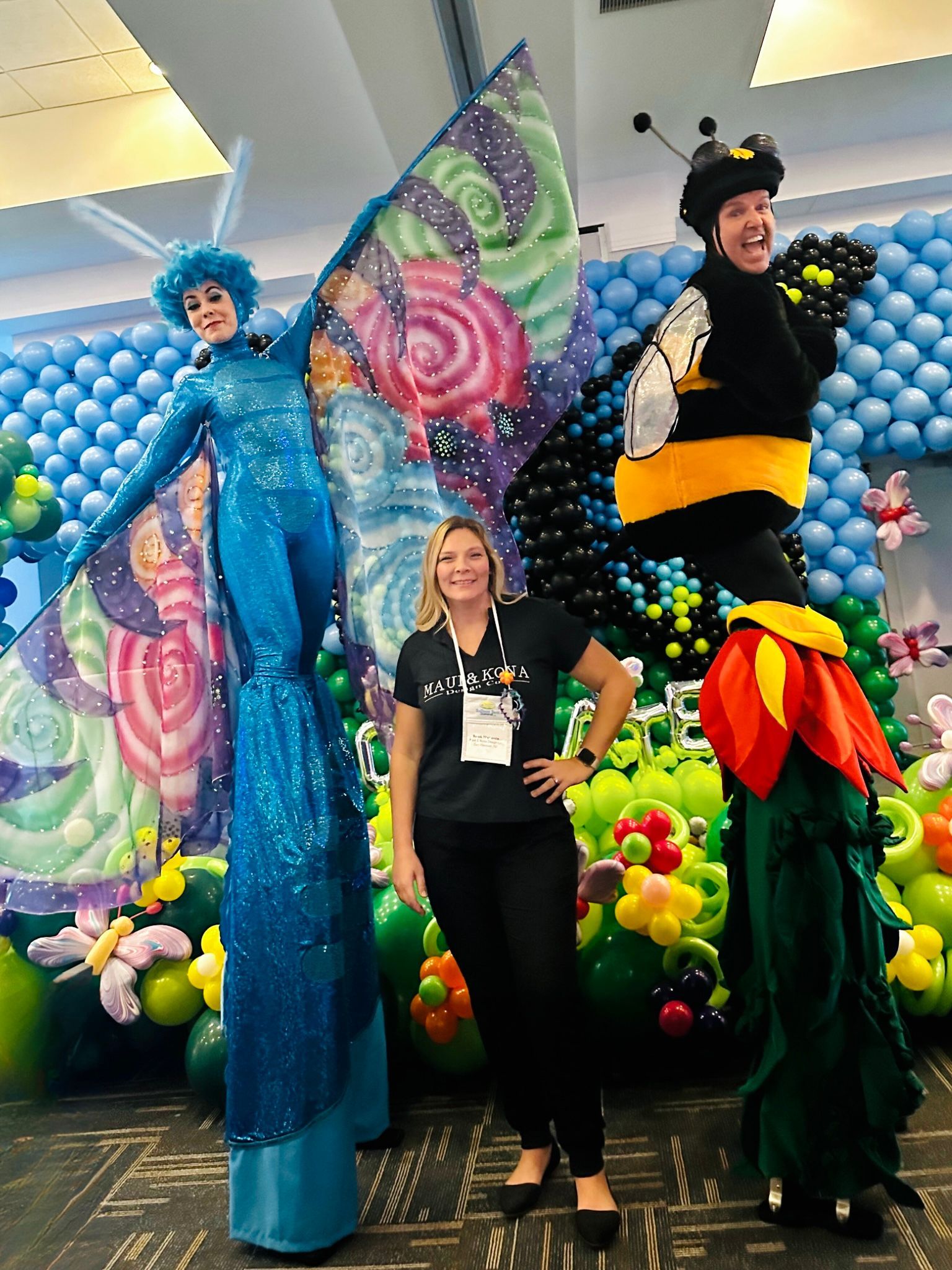 A woman is standing next to two people on stilts in front of balloons.