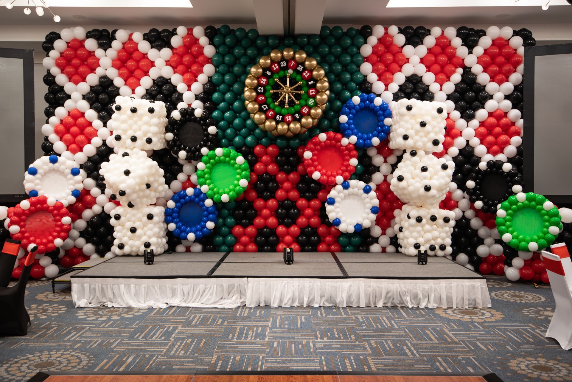 A wall made of balloons with poker chips and dice on it.