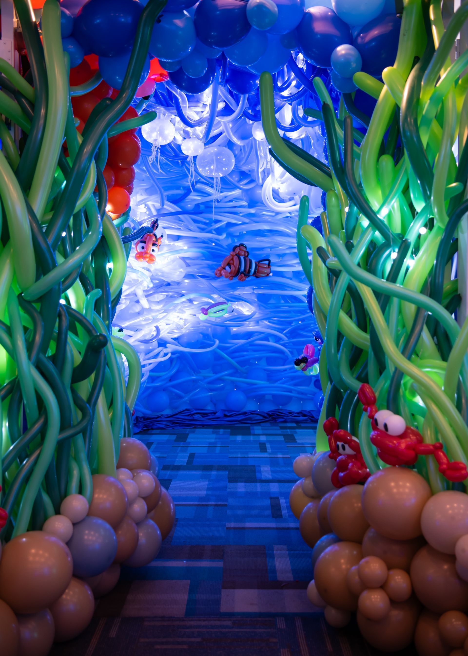 A tunnel made of balloons and seaweed leading to a pool.