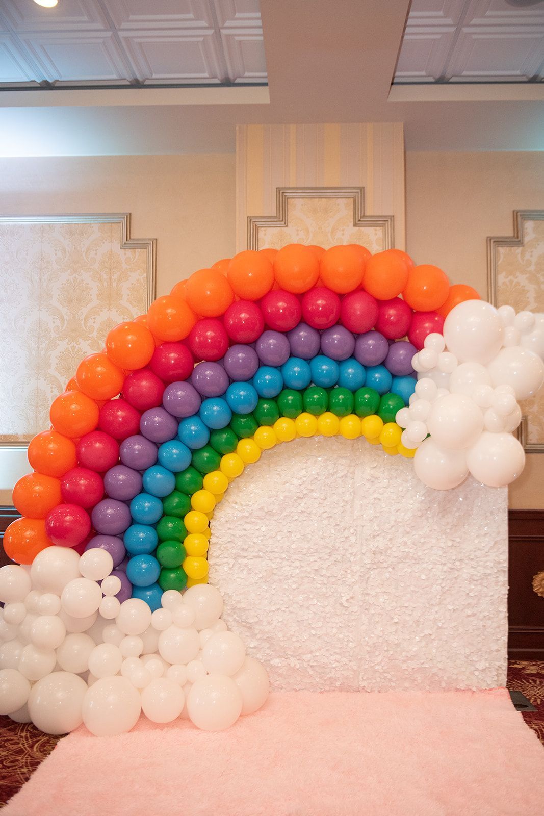 A rainbow made of balloons is sitting on top of a white wall.