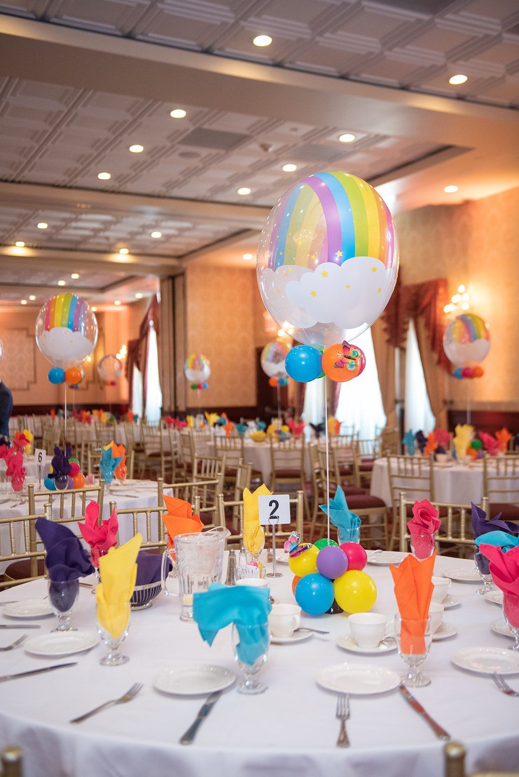 A room filled with tables and chairs decorated for a party with balloons.