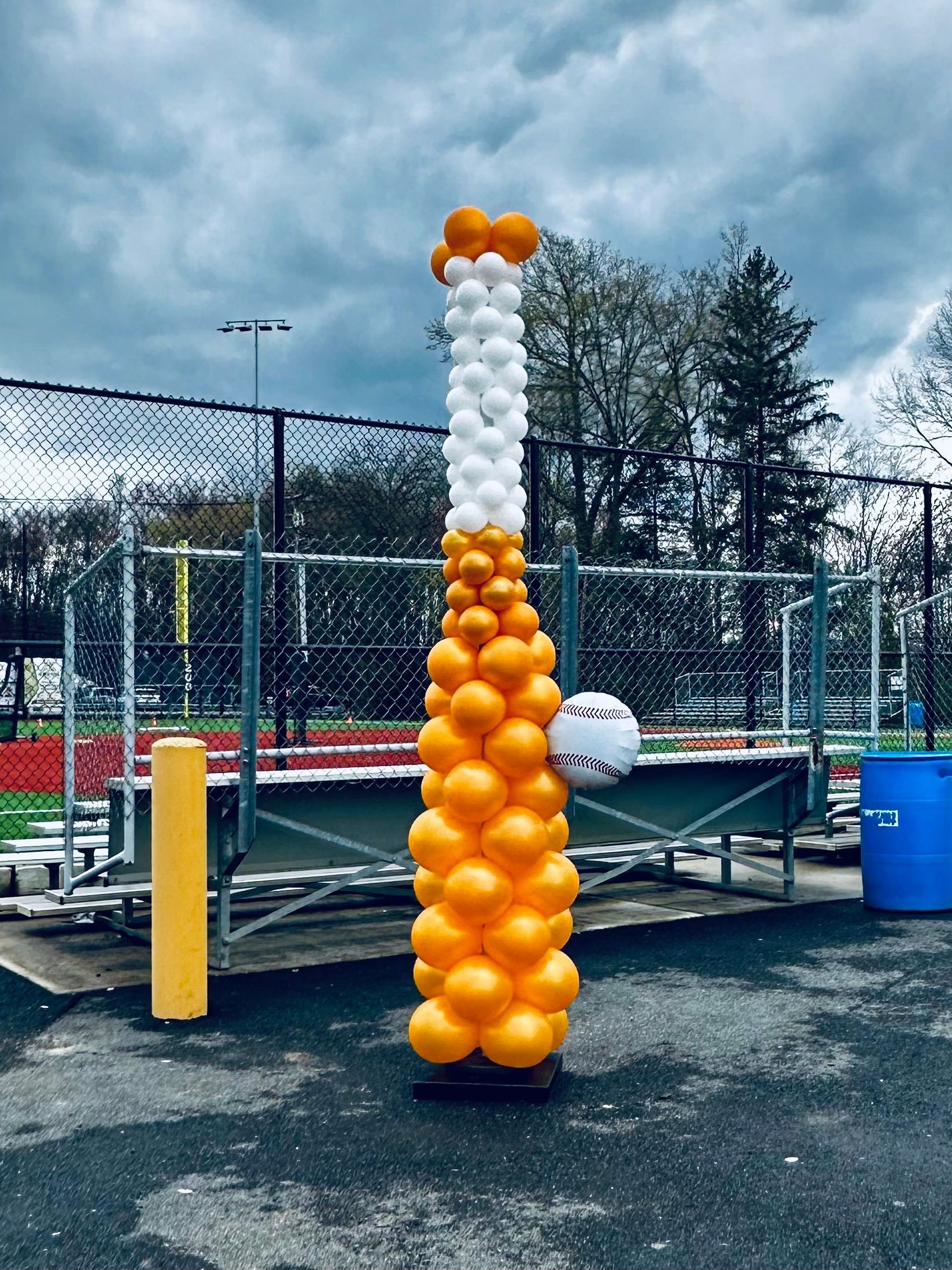 A balloon sculpture in the shape of a baseball bat is sitting in a parking lot.