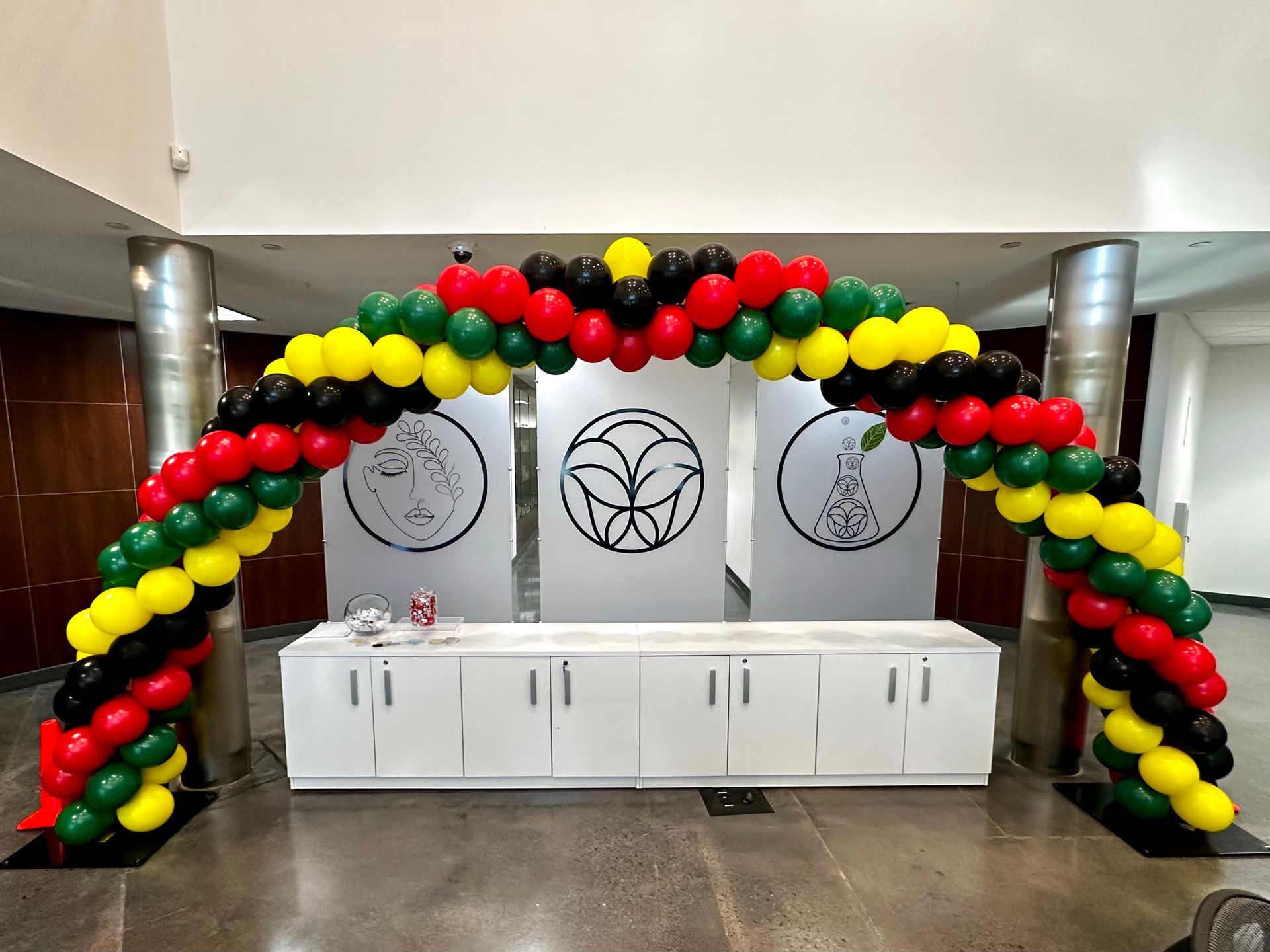 A large arch made of red , yellow , and black balloons in a room.
