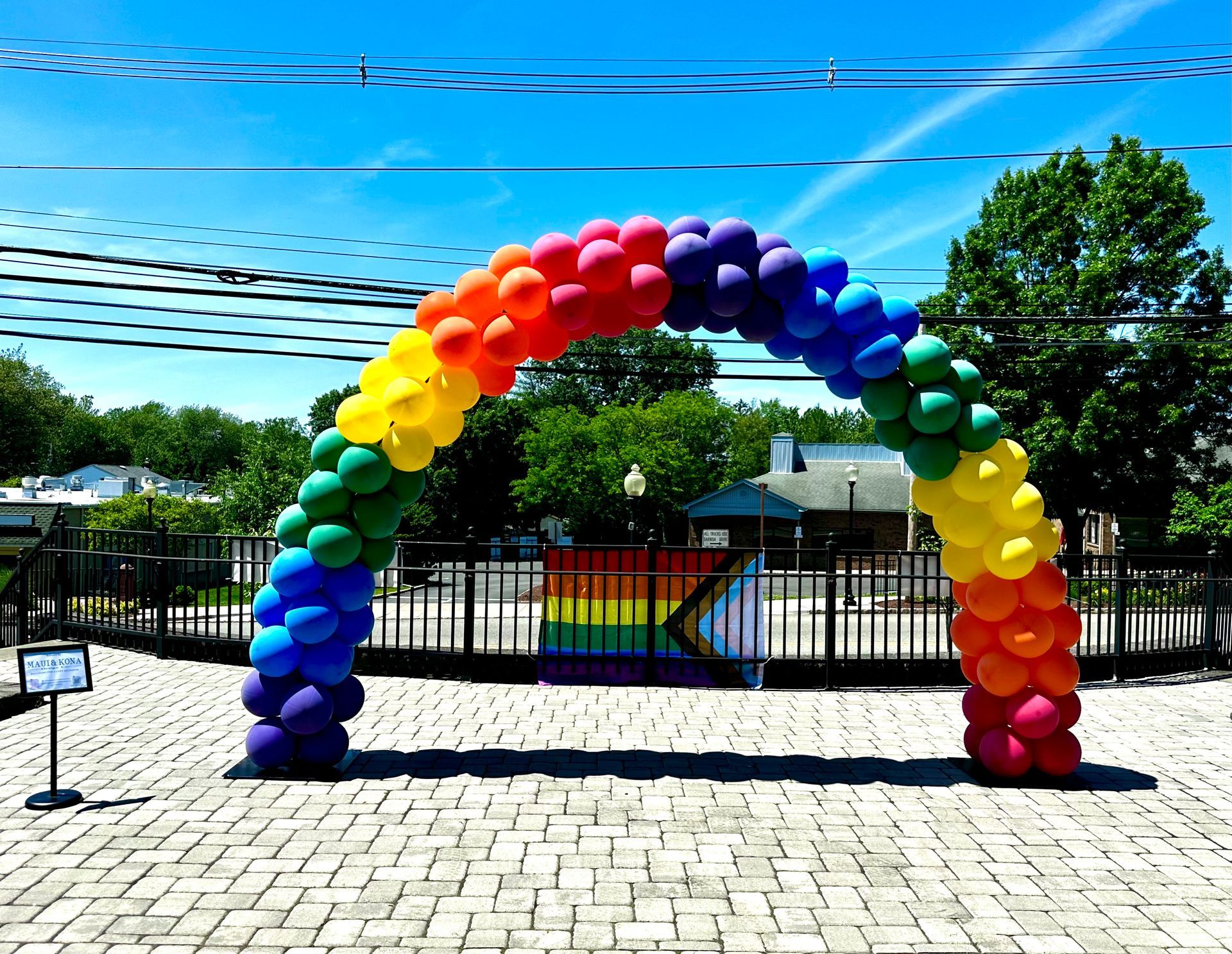 A rainbow colored balloon arch with a rainbow flag in the background