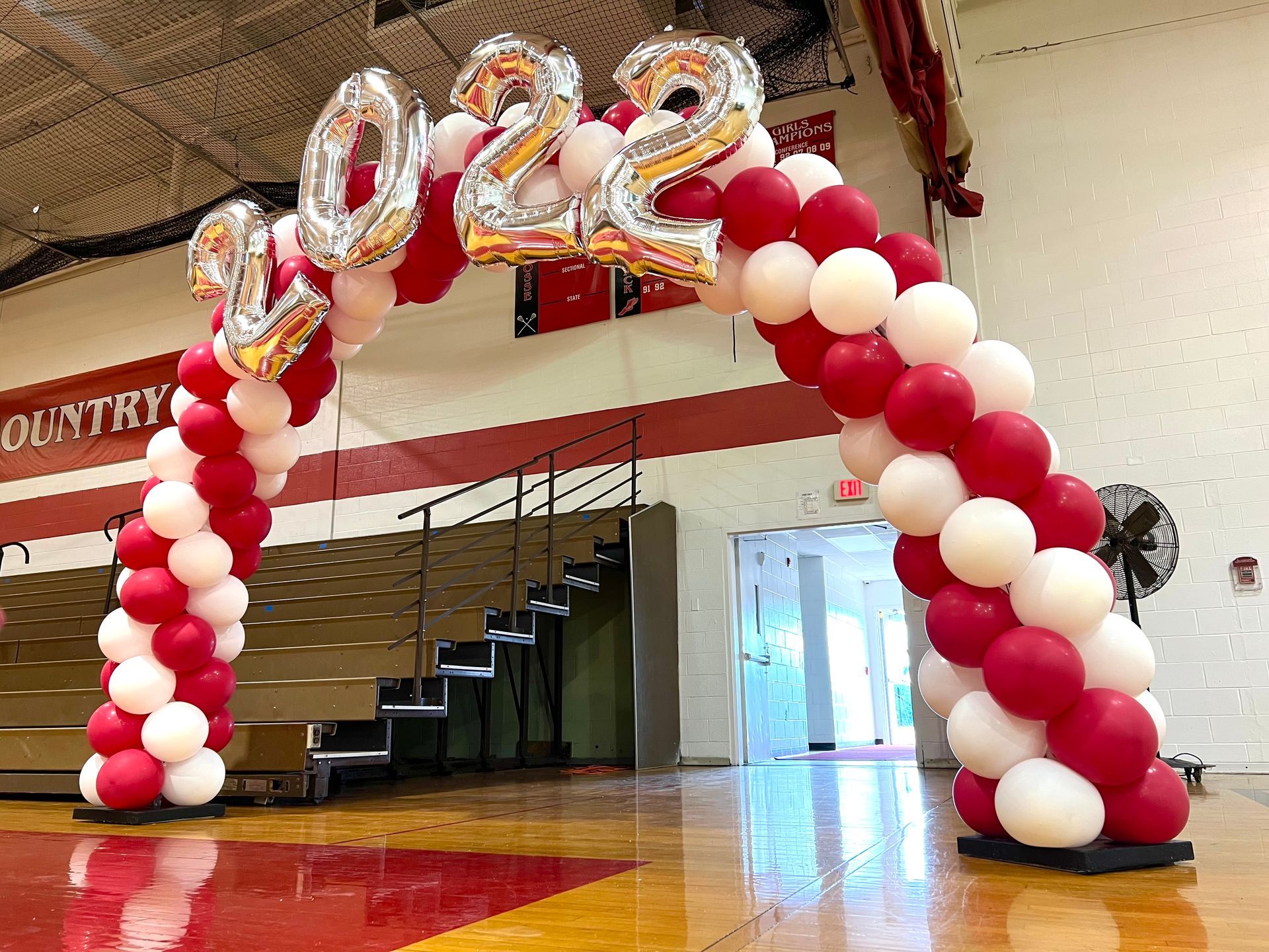 A large arch made of red and white balloons in a gym.