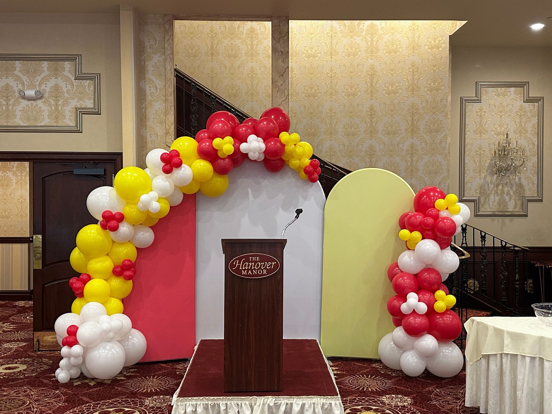 A room decorated with red , yellow and white balloons and a podium.