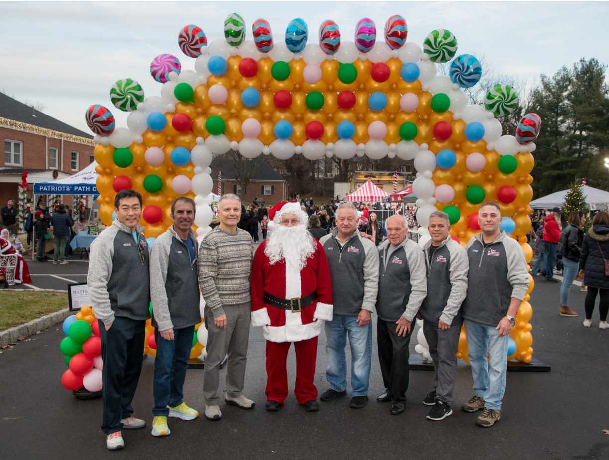 A group of men are posing for a picture with santa claus in front of a balloon arch.