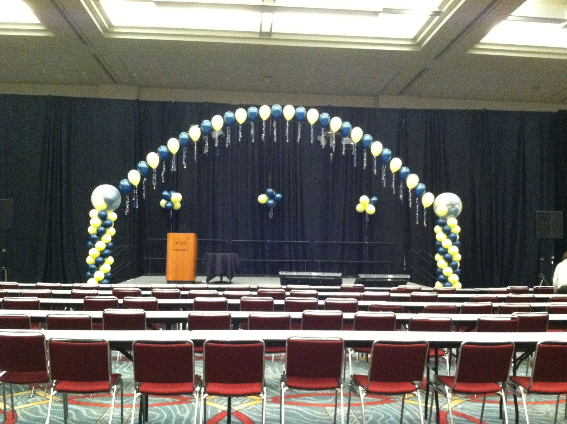 A room with tables and chairs and balloons on the stage