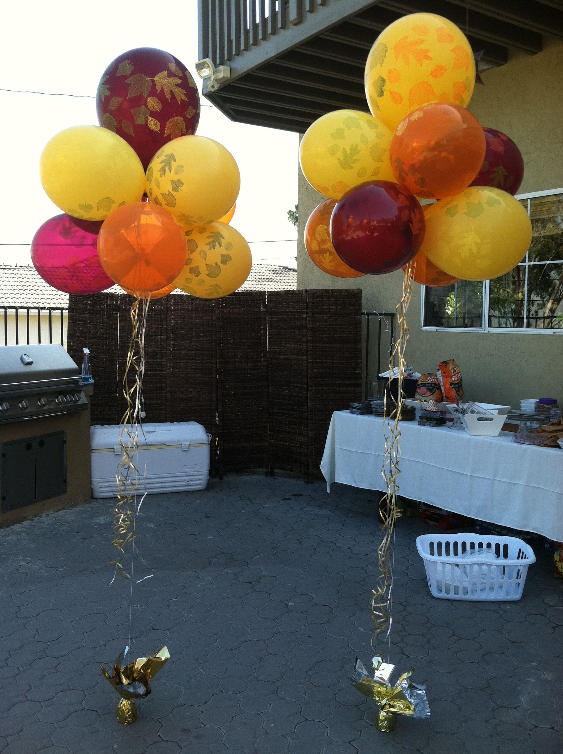 Two balloon bouquets: yellow, orange, and burgundy, at an outdoor party.