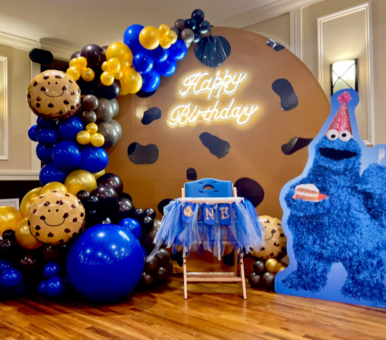 Cookie Monster-themed birthday party: balloon arch, cookie backdrop, high chair, Cookie Monster cutout.