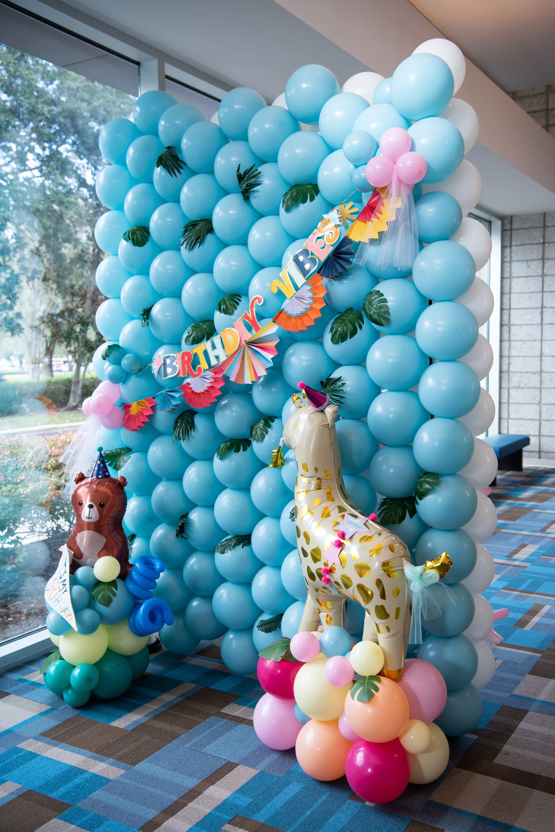 Balloon display with giraffe, bear, and blue wall, decorated with tropical accents.