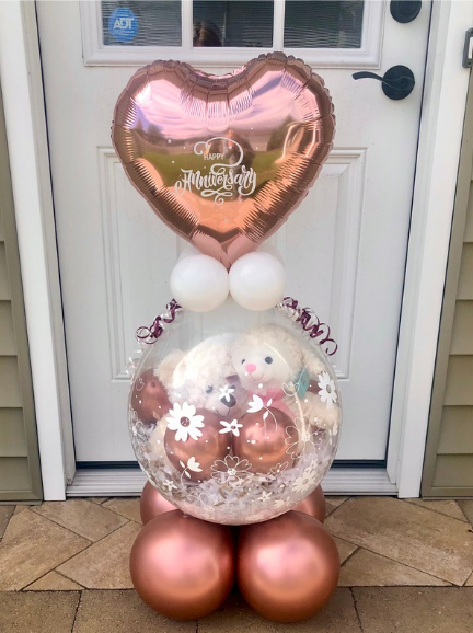 Rose gold balloon arrangement with a heart-shaped top, a clear orb, and round base, set against a white door.