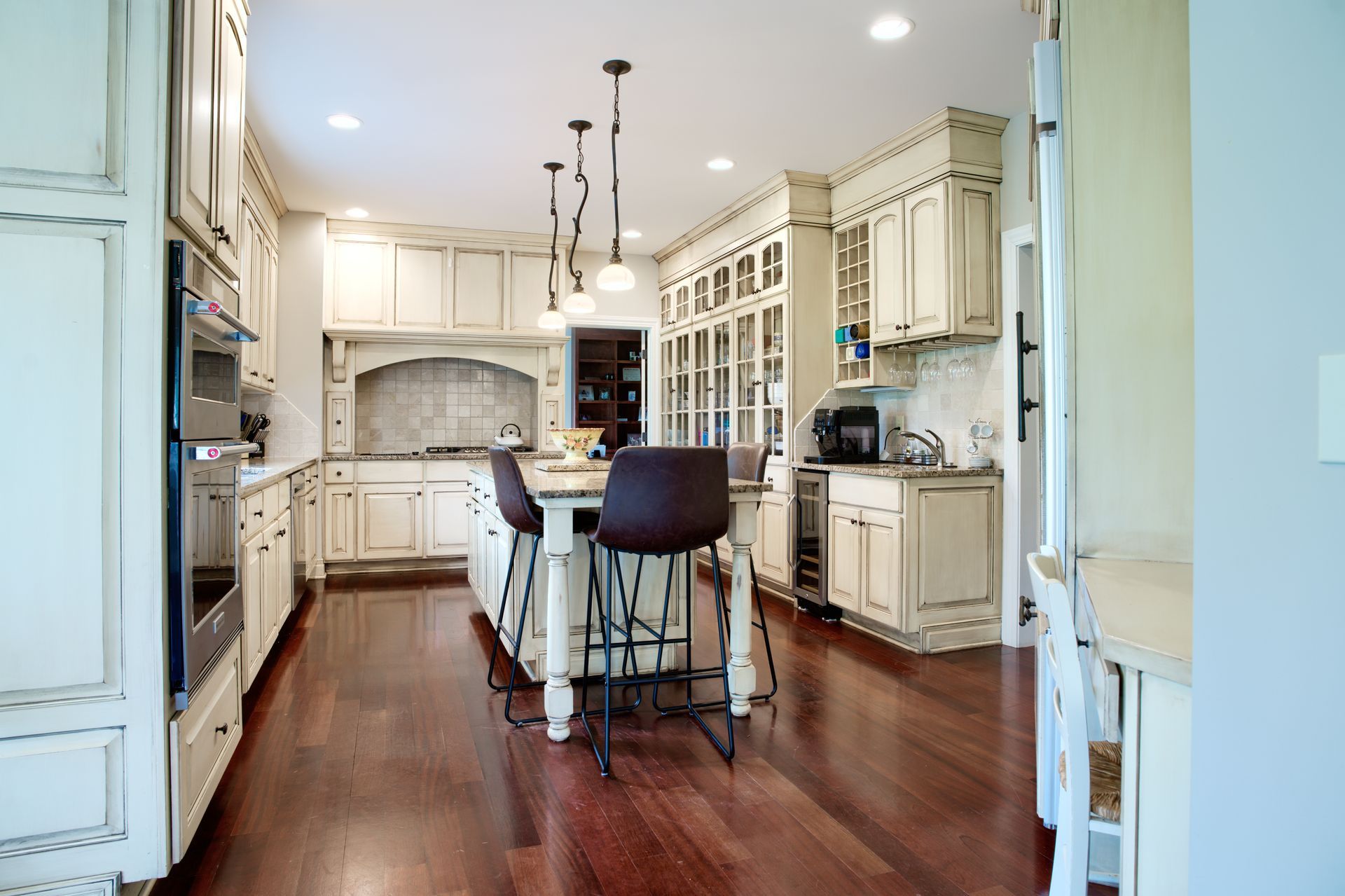 A kitchen with white cabinets , hardwood floors , stainless steel appliances and a large island.