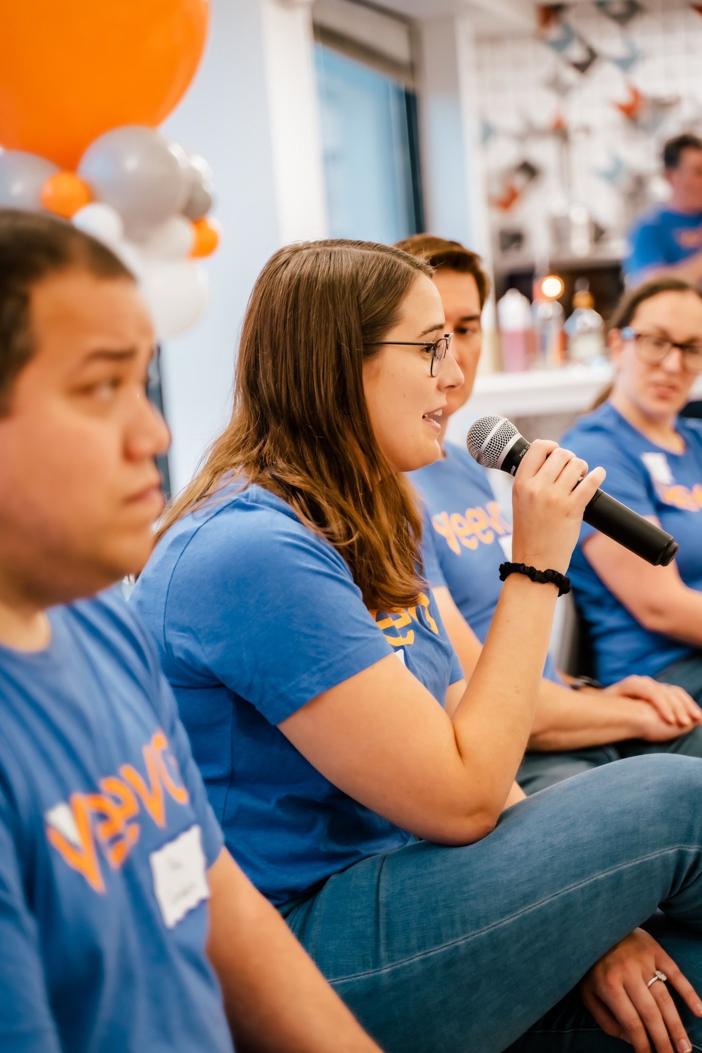 a woman is speaking into a microphone while sitting in front of a group of people .