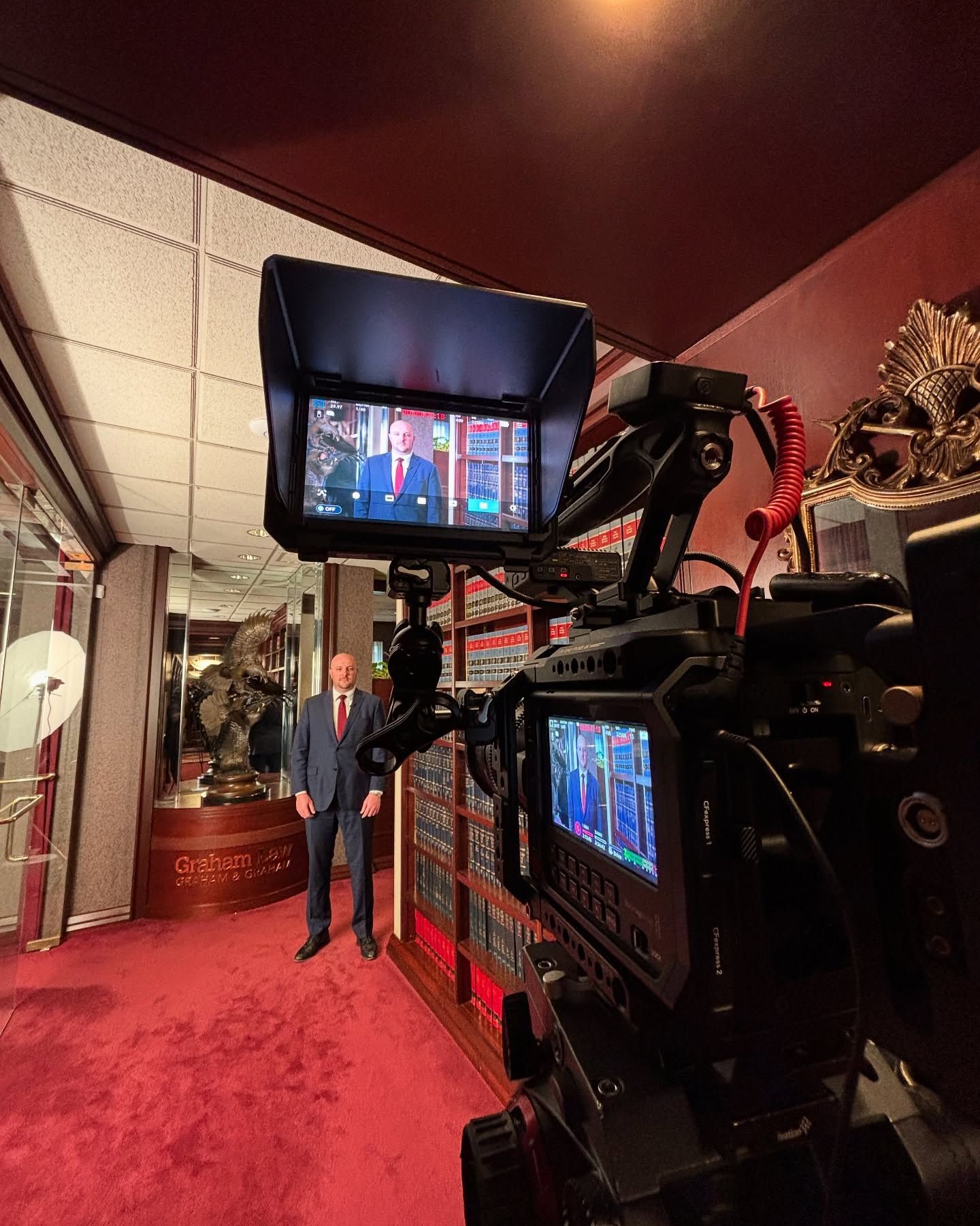 A camera is sitting on a wooden table in front of a computer monitor.