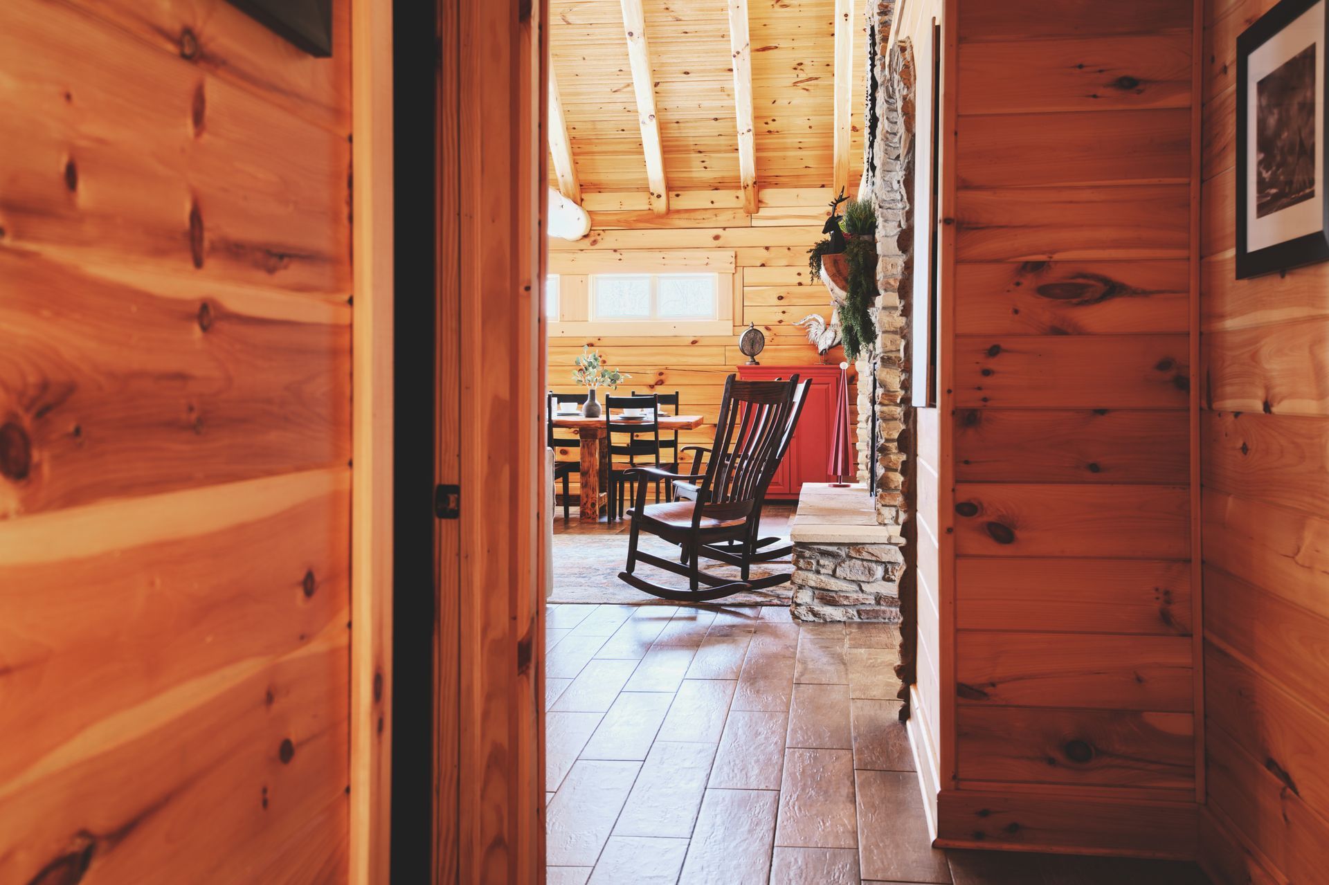 There is a rocking chair in the hallway of a log cabin.