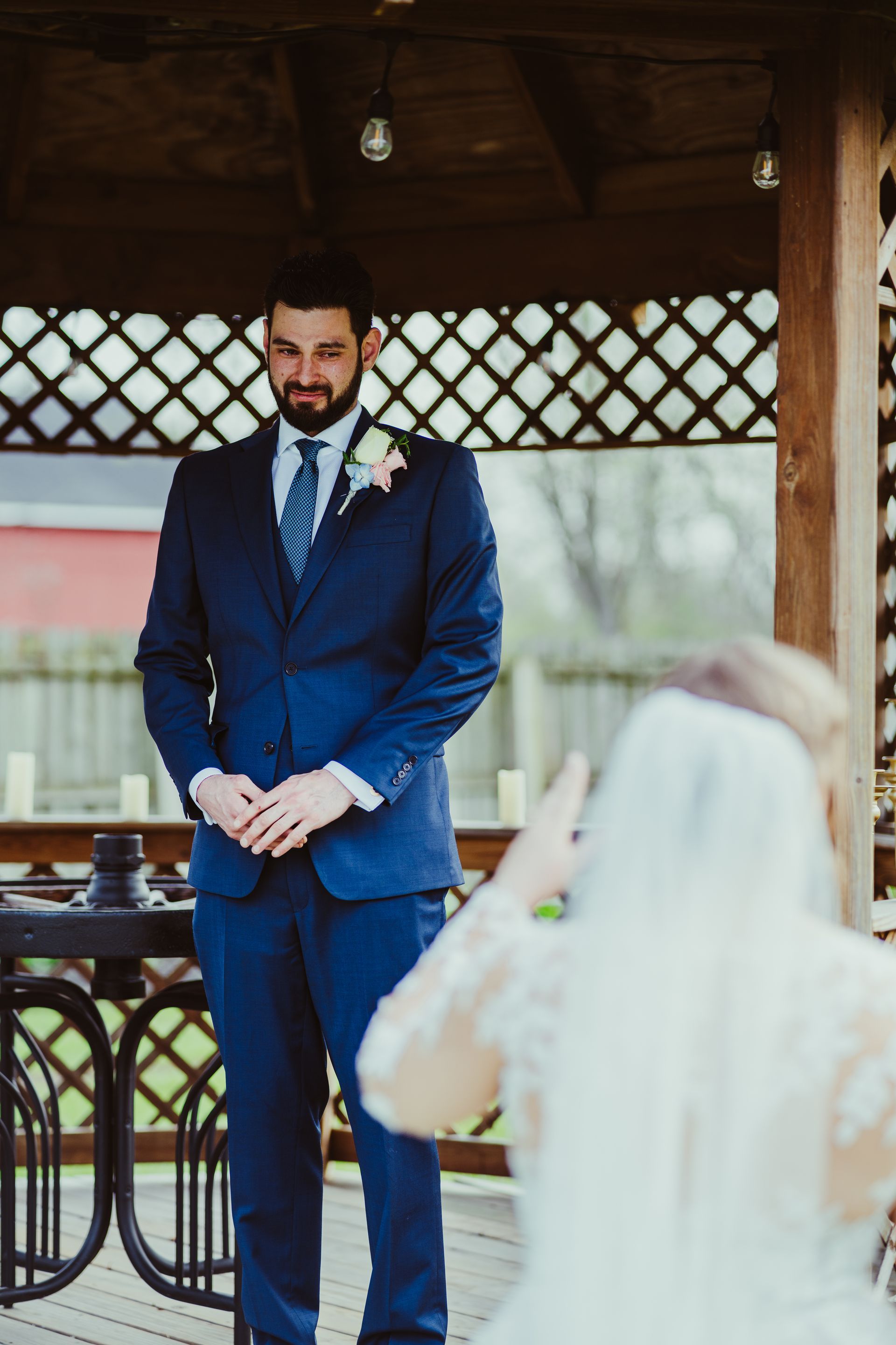 Groom in blue suit gazes at bride in a gazebo during a wedding ceremony.