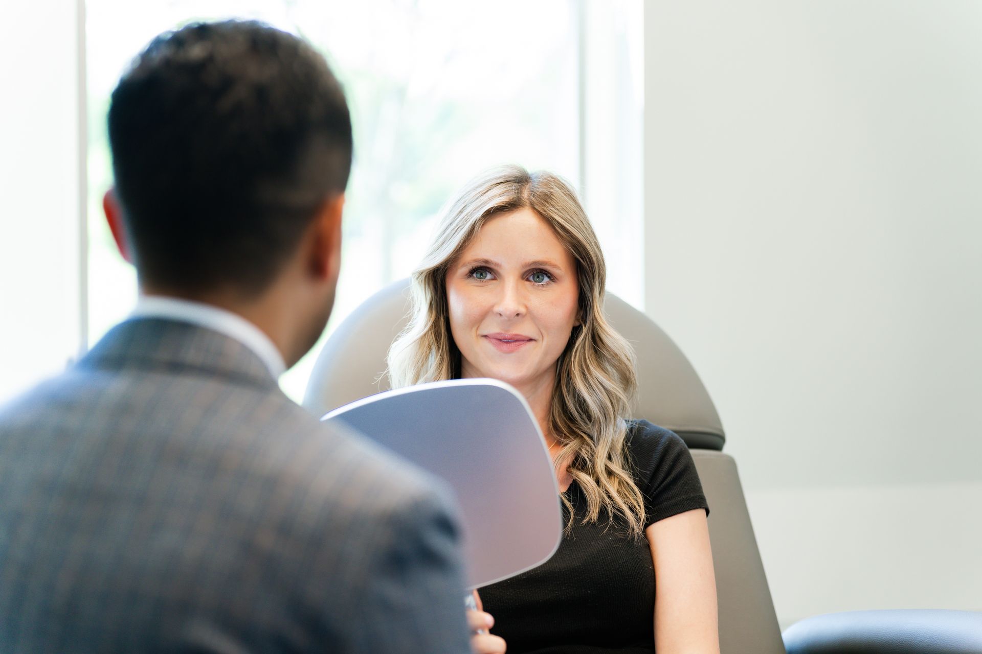 A woman is sitting in a chair talking to a man in a suit.