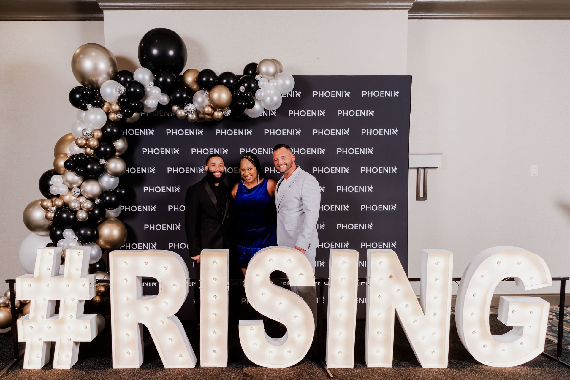 A group of people holding drinks stand and smile together in a brightly lit, indoor social gathering space.