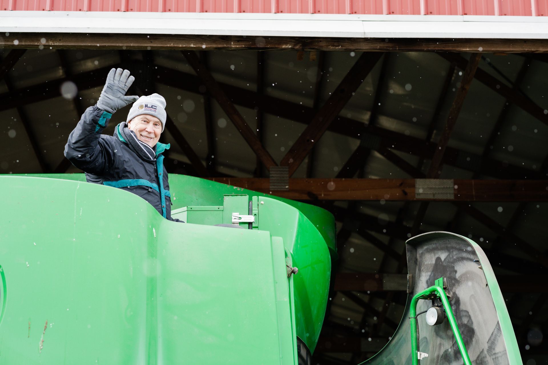 A man is waving from the back of a green tractor.