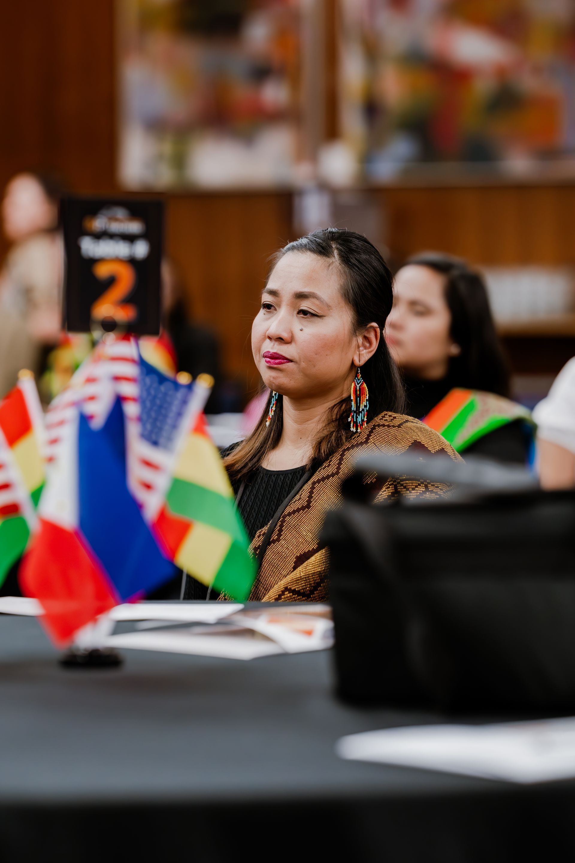 A woman is sitting at a table with flags in front of her.