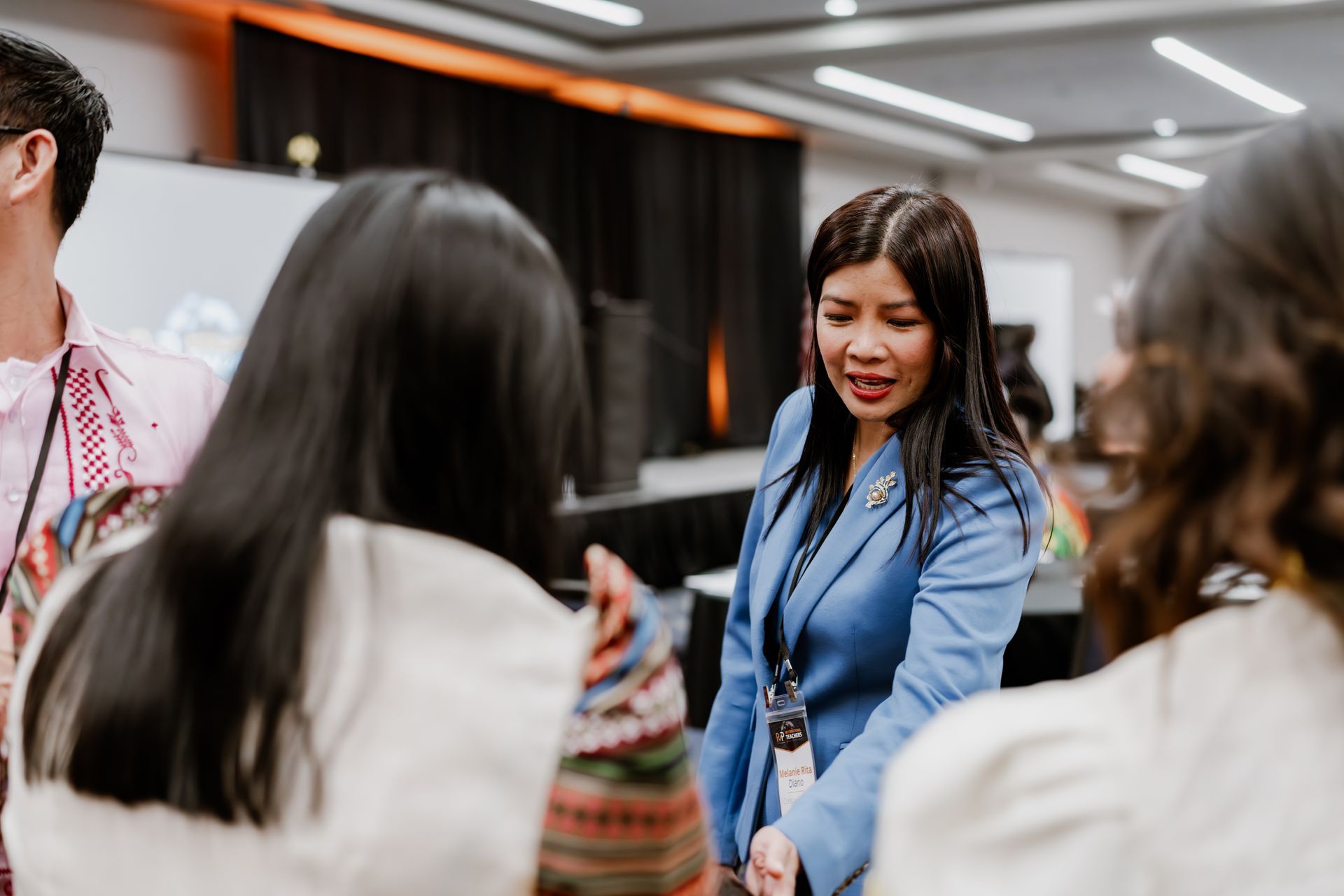A professional in a blue blazer speaks with others at an indoor conference or networking event.