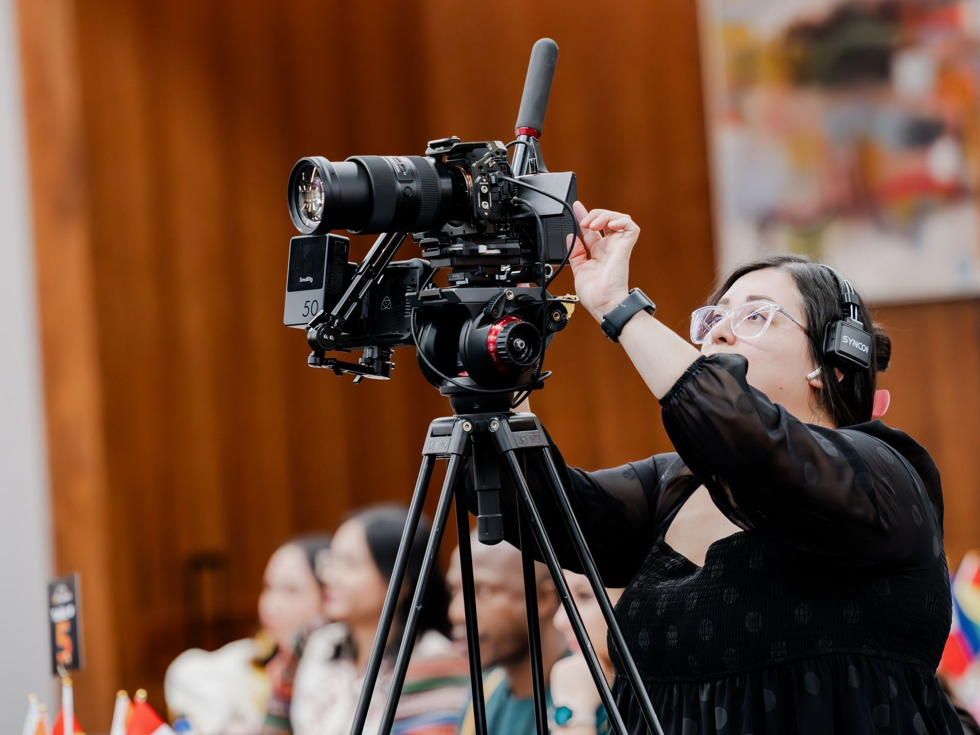 A woman is holding a camera on a tripod in front of a group of people.