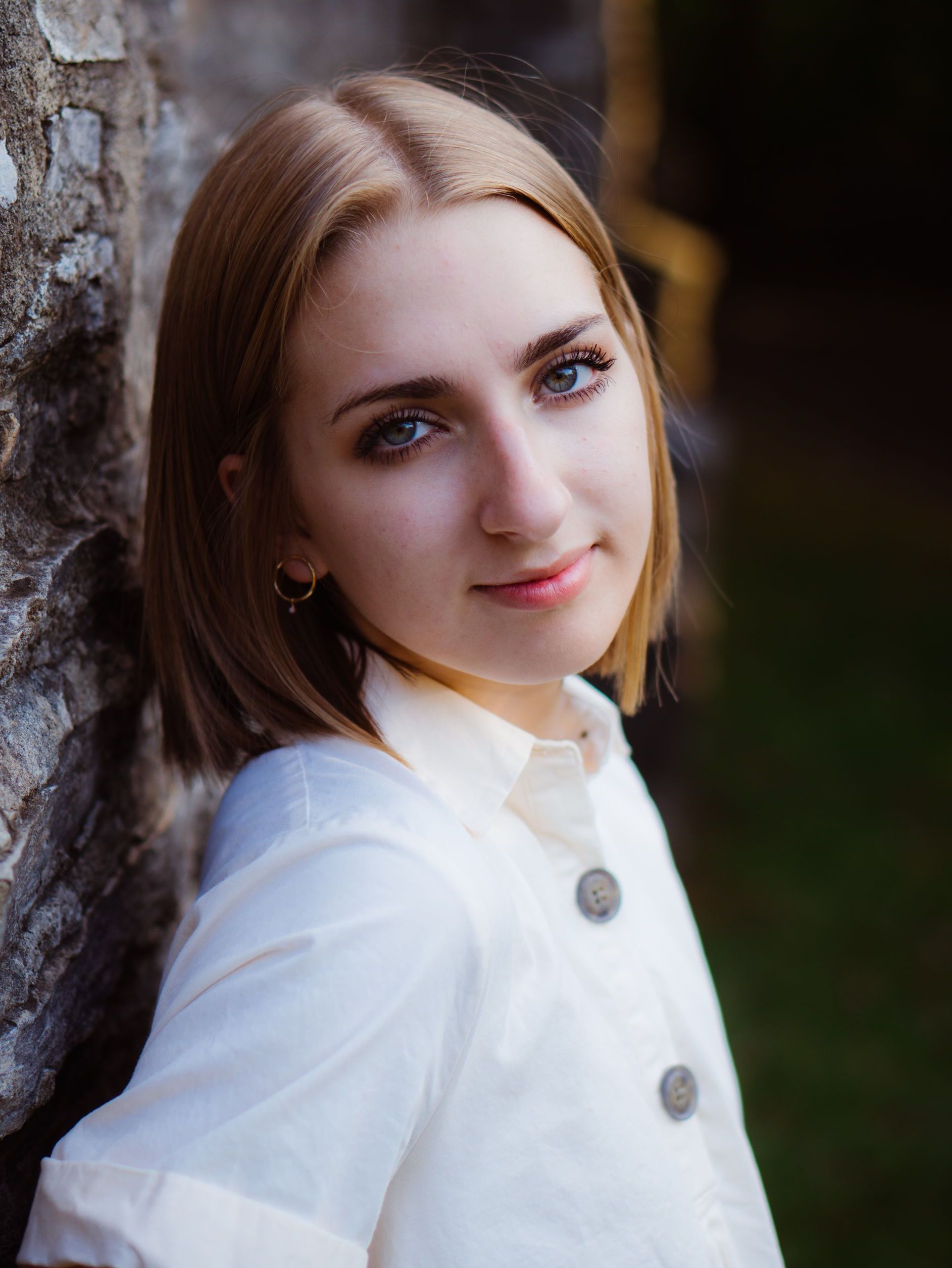 A high school senior in a white shirt is leaning against a wall .