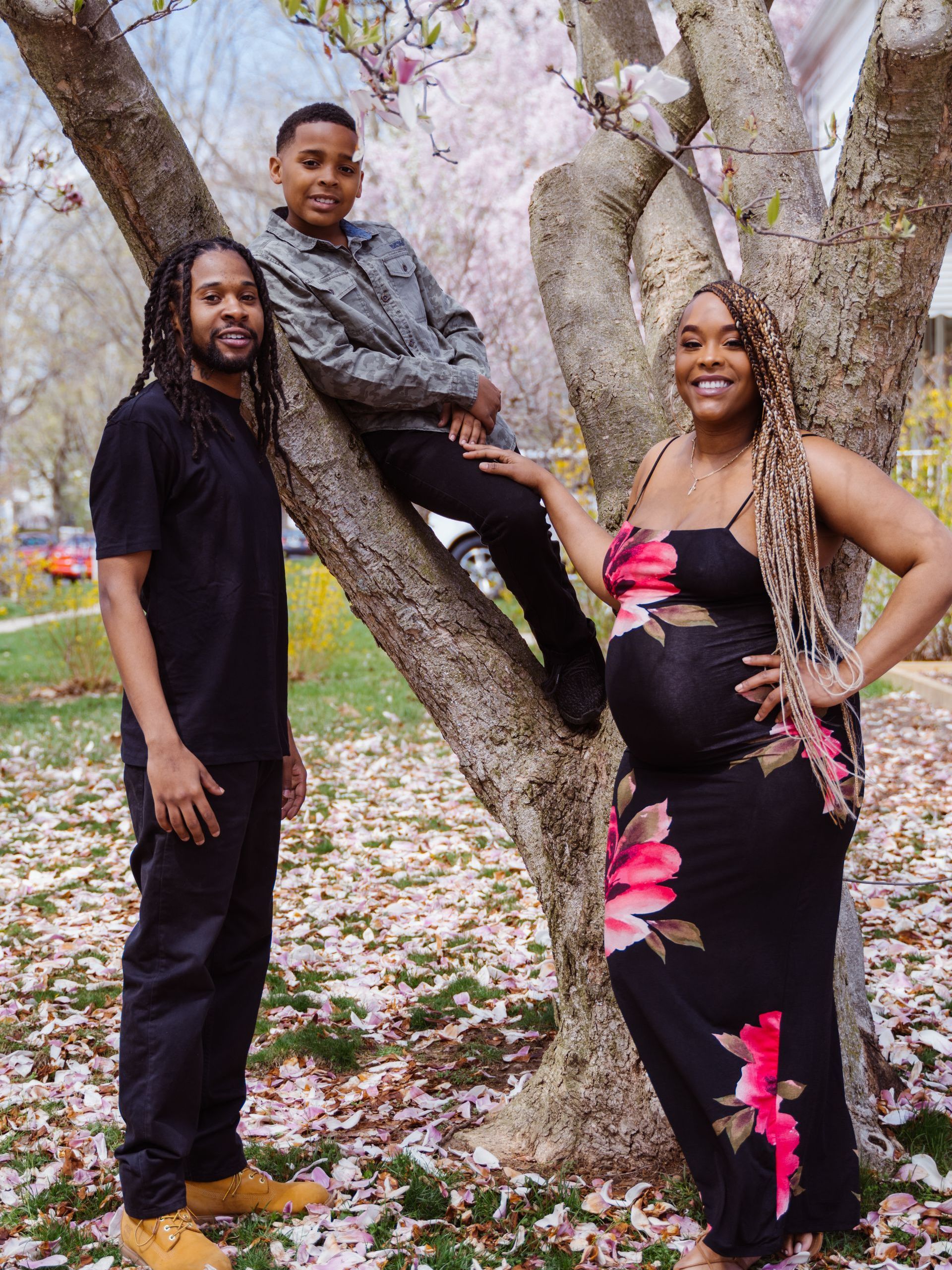 a pregnant woman is standing next to a man and a boy sitting on a tree .
