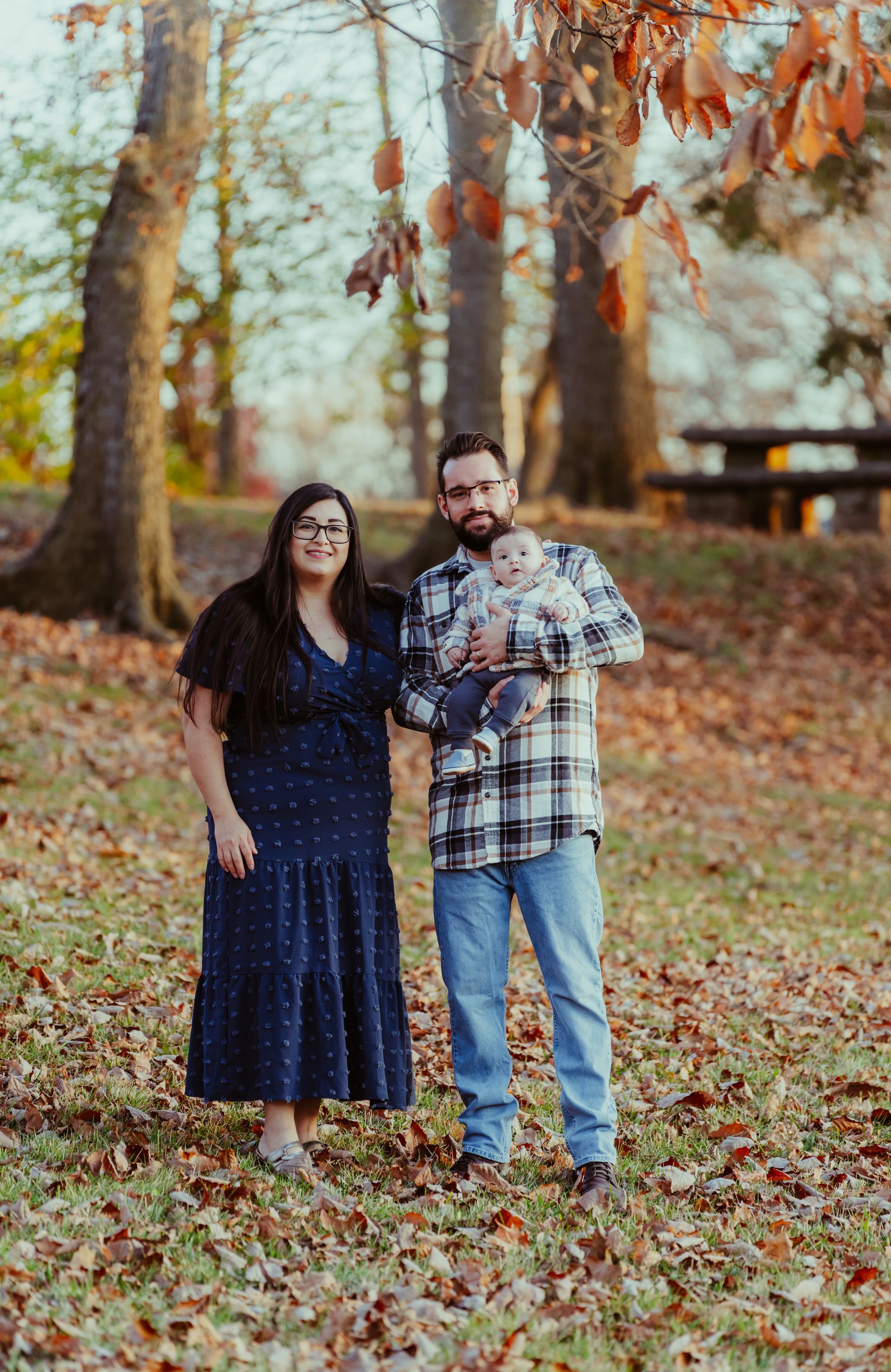 a man and woman are standing next to each other holding a baby in a park .