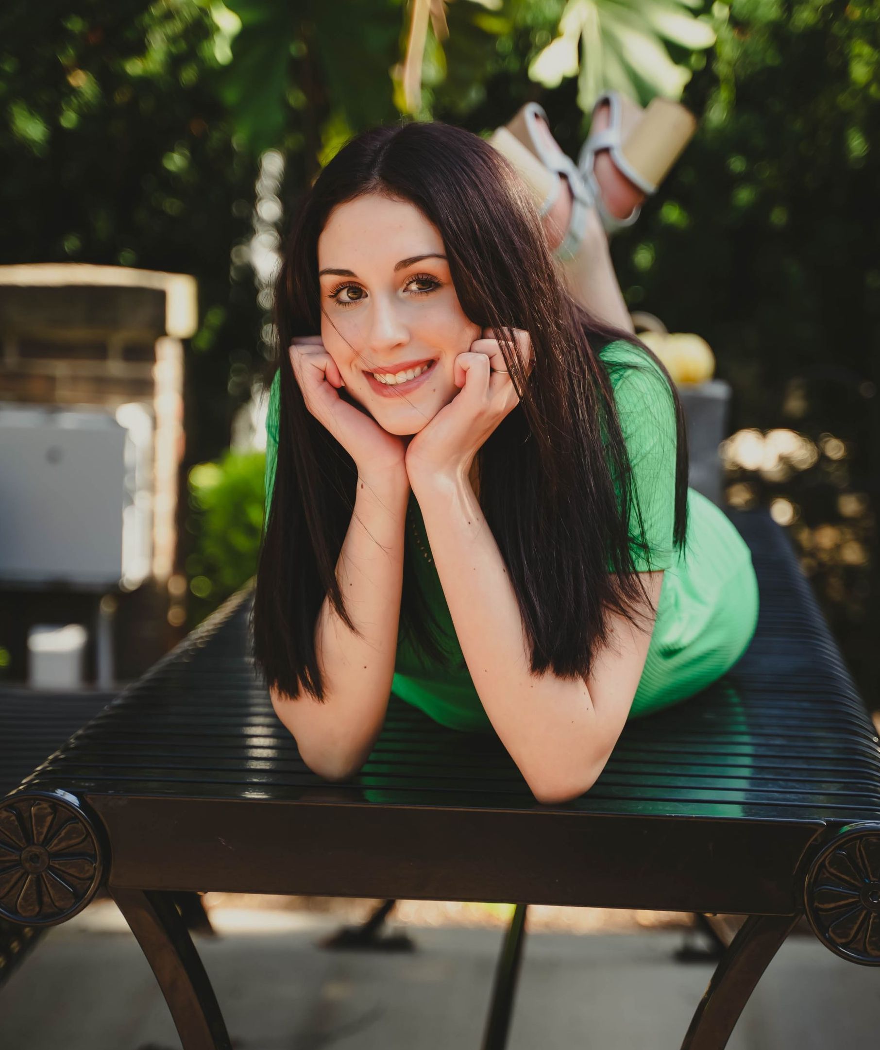 A high school senior in a green dress is laying on a table with her legs crossed .